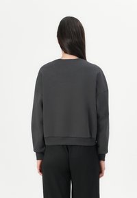 Felpa corta grigia scura con maniche lunghe, scollatura rotonda e polsi a costine. Texture liscia, design minimale, adatta per un abbigliamento casual.