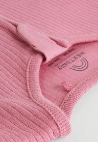 Rosa gerippter Babysweater mit Rundhalsausschnitt, ausgestattet mit einem kleinen Etikett innen, aus weichem Stoff mit leichtem Stretch.