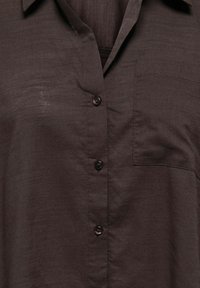 Chemise boutonnée marron foncé avec col, poche sur la poitrine gauche et tissu texturé avec une finition légèrement brillante.