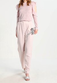 Haut rose clair avec manches à volants et découpes aux épaules, associé à un pantalon rose ample assorti et des sandales à talons argentées.