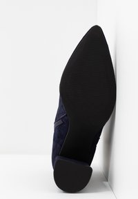 Chaussure à talon haute en suedine marine avec un bout pointu et une semelle en caoutchouc noir texturé. Dotée d'une fermeture éclaire sur le côté.