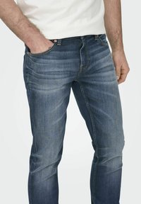 Tumedat sinised denim püksid kitsas lõikes, klassikalise viie tasku disainiga ja kerge kulumisega reite piirkonnas.
