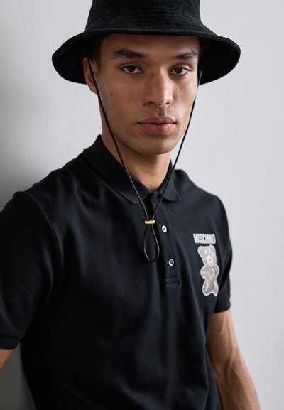 Black polo shirt with bear graphic, featuring a classic collar and button placket. Paired with a black bucket hat with ties.