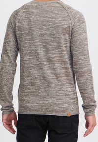 Pull en maille à manches longues texturé de couleur marron et beige, avec un col rond et des manches raglan. Détail de l'étiquette remarquable au niveau de l'ourlet.