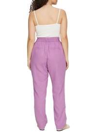 Pantalons en lin lilas avec une coupe décontractée, taille élastique, deux poches arrière et une texture lisse, associés à un top blanc à fines bretelles.