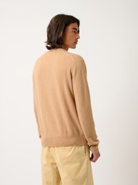 Beiger Kaschmirpullover mit langen Ärmeln, gerippten Bündchen und Saum. Glatte Textur und traditionelles Rundhalsdesign. Getragen mit hellgelben Hosen.