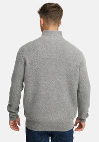 Mand iført en lysegrå ribstrikket sweater med høj krave, vist fra ryggen, parret med mørkeblå jeans.