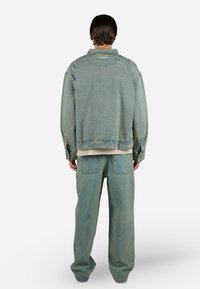 Chaqueta de mezclilla azul claro con un corte relajado, que presenta un gran collar, hombros caídos y un par de pantalones a juego con corte recto.