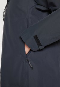 Dark navy waterproof jacket featuring a side pocket, adjustable cuffs with Velcro, and a drawstring hem for secure fit. Smooth texture.