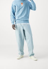 Sudadera de color azul claro con el logo de PUMA, combinada con unos pantalones vaqueros holgados de color denim claro y zapatillas blancas. Tejido suave y corte relajado.
