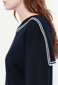 Pull en maille marine avec un large col de marin rayé blanc. Le tissu en tricot est lisse, avec une coupe décontractée et des manches courtes.
