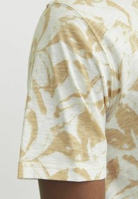 Camiseta de manga corta con un patrón abstracto beige sobre un fondo claro, con una tela suave y texturizada y un cuello redondo.