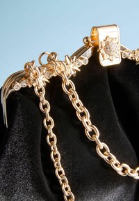 Poc̆eaua din catifea neagră, cu un cadru din metal auriu, având un sistem de închidere în formă de floare, lantĭ decorative și accente din pietricele transparente.