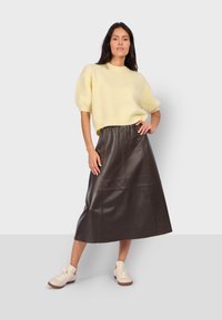 Pull en maille jaune à manches courtes, avec une coupe décontractée, associé à une jupe midi en cuir plissé marron foncé et des baskets claires.