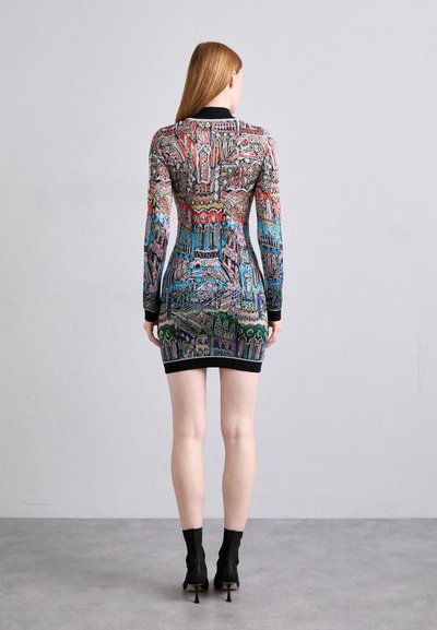 Robe mini cintrée avec un motif architectural coloré, manches longues, décolleté rond, et bord noir. Portée avec des bottes à talons arrivant aux chevilles.