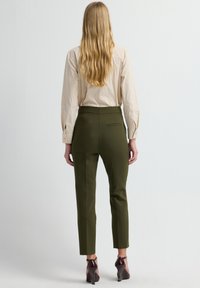 Olivgrüne, maßgeschneiderte Hose mit hohem Bund, figurbetonter Passform und einer Gesäßtasche, kombiniert mit einem beigen Langarmhemd.