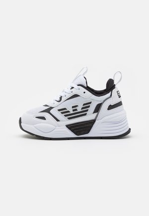 Baskets athlétiques blanches et noires avec dessus en mesh, fermeture à lacets, semelle épaisse et logo ailé sur le côté.