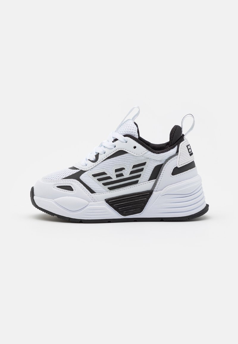 Baskets athlétiques blanches et noires avec dessus en mesh, fermeture à lacets, semelle épaisse et logo ailé sur le côté.