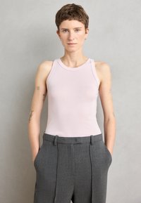 Rosa ermeløs topp med en tettsittende design, laget av glatt stoff. Kombinert med høytlivs grå bukser med skarpe folder og lommer.