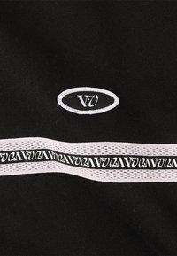 Tela negra con un parche de logo blanco destacado en forma ovalada y una banda blanca con rayas horizontales que tiene un diseño de texto negro repetido.