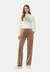 Felpa color crema con una grafica centrale, abbinata a pantaloni tuta in morbido velluto marrone. Entrambi hanno una vestibilità comoda e dettagli con cordino.