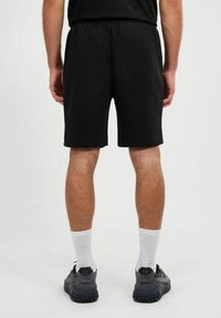 Pantalones cortos deportivos negros con una cintura elástica, que llegan a la mitad del muslo, combinados con calcetines blancos y zapatillas oscuras. Tejido suave con un detallado mínimo.