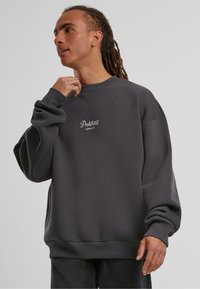 Grå crewneck sweatshirt lavet af blødt stof. Har et tætsiddende ærme og kant, med "Forbudte Beklædningsgenstande" broderet på brystet.