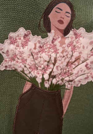 Kobieta z zamkniętymi oczami trzyma różowe haftowane kwiaty na tle zielonej dzianiny.