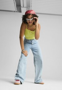 Canottiera a coste gialla, jeans larghi blu chiaro, fascia per capelli rossa a fantasia, occhiali da sole grigi, sneakers beige con dettagli rossi, collana di perline.