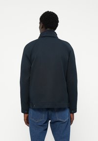 Navy blue jacket with a collared neck, buttoned cuffs, and a smooth texture. Raglan sleeves and a plain design without patterns.
