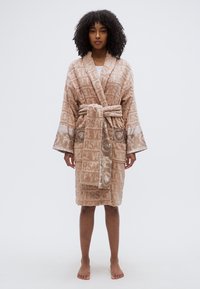 Μπεζ ρόμπα κατασκευασμένη από απαλό ύφασμα, με ανάγλυφα μοτίβα λογότυπου, φαρδιά μανίκια, ζώνη που δένει και διακοσμητικές λεπτομέρειες στις μανσέτες.