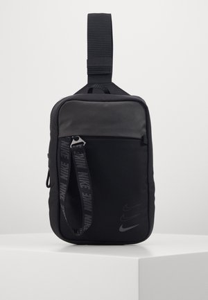 Sac bandoulière rectangulaire noir avec poche zippée à l'avant, sangle réglable et logos Nike swoosh dans le coin inférieur droit.