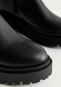 Zwarte leren enkellaarzen met een ronde neus en een gestructureerde afwerking. Dikke, robuuste zolen met een uitgesproken profiel voor grip.