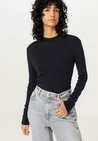 Langärmliges, enganliegendes Oberteil in einheitlichem Marineblau aus weichem Stoff. Getragen mit high-waist, hellblauen Jeans im klassischen Fünf-Taschen-Design.