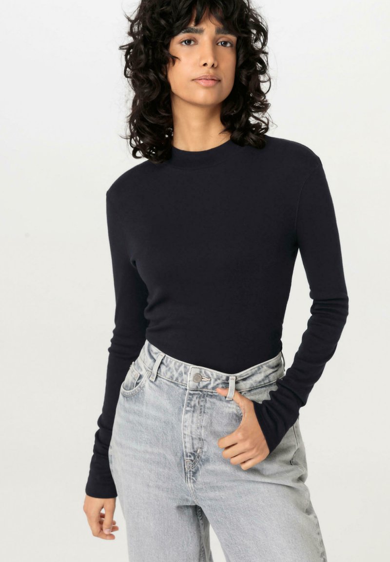 Langärmliges, enganliegendes Oberteil in einheitlichem Marineblau aus weichem Stoff. Getragen mit high-waist, hellblauen Jeans im klassischen Fünf-Taschen-Design.