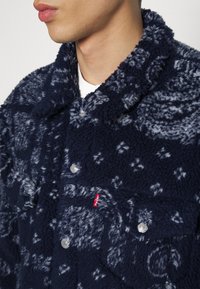 Giacca in pile blu navy con motivi astratti bianchi, bottoni a pressione e un'etichetta rossa Levi's sul taschino sinistro.