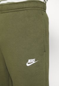 Olivgröna Nike-mjukisbyxor i mjuk bomullsblandning, med en vit broderad logotyp på sidan, elastisk midjeresår och fickor.