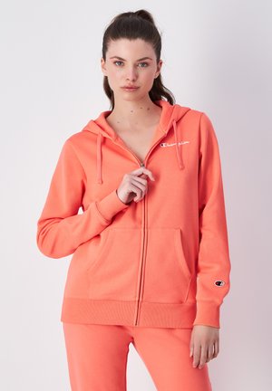 Koralle Zip-Hoodie aus weichem Stoff mit einer Fronttasche, verstellbarem Kordelzug in der Kapuze und einem Logo auf der Brust und dem Ärmel.