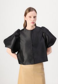 Schwarzes Satin-Cropped-Top mit Puffärmeln, runder Ausschnitt und verdecktem Knopfverschluss, kombiniert mit einem beigen Rock.