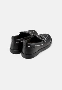 Scarpe in pelle nera con una finitura liscia, caratterizzate da cuciture bianche a contrasto e un design slip-on. Punta tonda e suola in gomma bassa.