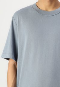 Camiseta de algodón azul claro con cuello redondo, mangas cortas y detalles de costura visibles, que presenta una textura suave y lisa.