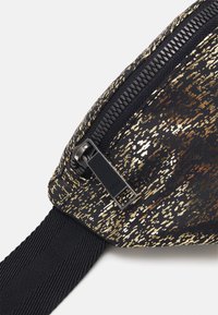 Zwarte tas met gouden en bronzen spikkels, voorzien van een zwarte rits en een gestructureerde riem. Glad materiaal met een modern ontwerp.