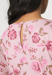 Růžová květinová blůza s průstřihovým vzadu a knoflíkovým zapínáním, vyrobená z lehké látky, zdobená vzory růží a listů.