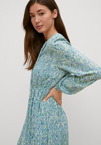 Abito con motivo floreale in una palette di colori blu-verde, maniche lunghe a sbuffo e vita cintrata. Tessuto morbido con una silhouette fluida.