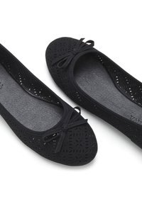 Schwarze Ballerinas mit ausgeschnittenen Mustern, abgerundeter Spitze und kleinen Schleifendetails an der Front. Weiches Material mit strukturiertem Fußbett.