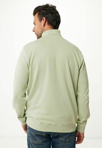 Suéter verde claro con un cuello alto, textura suave, puños y dobladillo acanalados. La vista trasera muestra un diseño simple y limpio con un corte relajado.