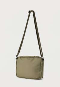 Χιαστί τσάντα σε ελιά από πράσινο, με ορθογώνιο σχήμα, κατασκευασμένη από ανθεκτικό ύφασμα. Διαθέτει ρυθμιζόμενο λουρί και ομαλή, υφή επιφάνεια.