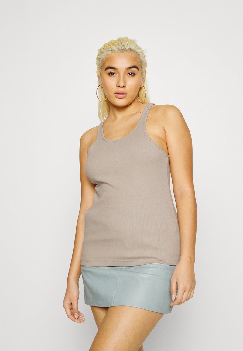 Top de alças largas em bege com nervuras, combinado com uma saia mini de couro azul claro. Modelo posa em frente a um fundo branco simples.