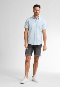 Cămășă bleu deschis cu mânecă scurtă și nasturi, din bumbac, asociată cu pantaloni scurți gri închis cu tiv rulat și adidași albi. Design simplu, ajustat.