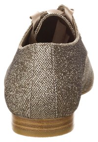 Dos de chaussure en bronze brillant avec une surface texturée, doublure douce et un talon en bois bas ; présente un ruban en tissu pour un détail supplémentaire.